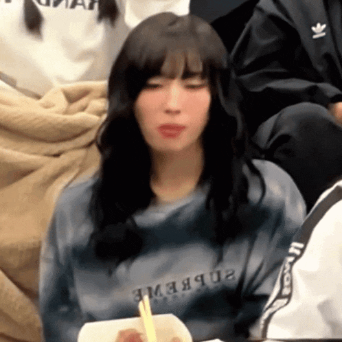 a woman wearing a shirt that says ' supreme ' on it is eating with chopsticks