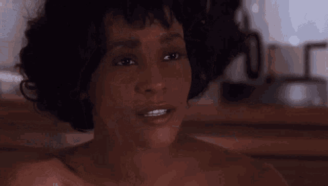 a woman without a shirt is making a funny face while sitting in a bathtub .
