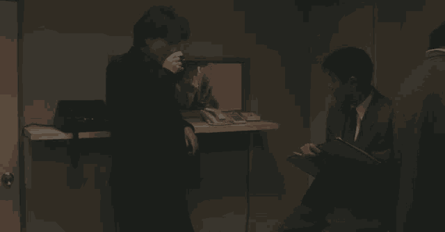 two men are standing next to each other in a dark room talking on a cell phone .