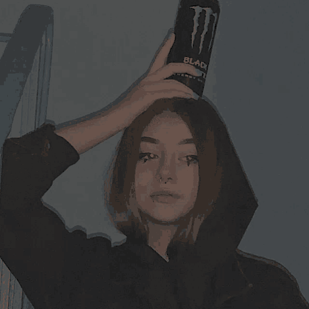 a girl is holding a can of monster energy drink on her head