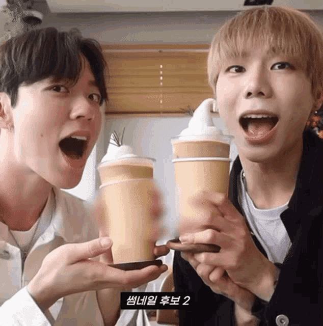 two young men are holding cups of coffee in their hands and one of the cups has a swirl of whipped cream on top