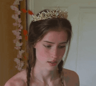 a young woman wearing a tiara and braids is looking at the camera .