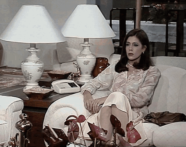a woman sits on a couch with two lamps and a telephone