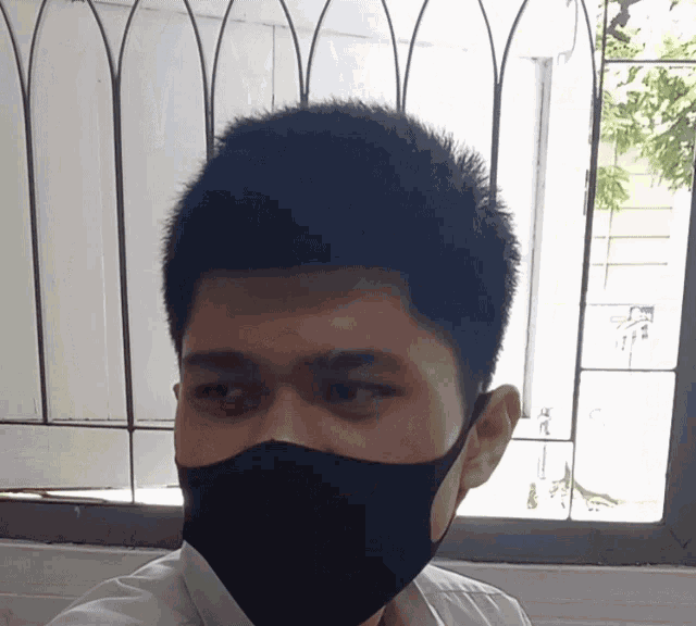 a man wearing a black face mask is looking out a window