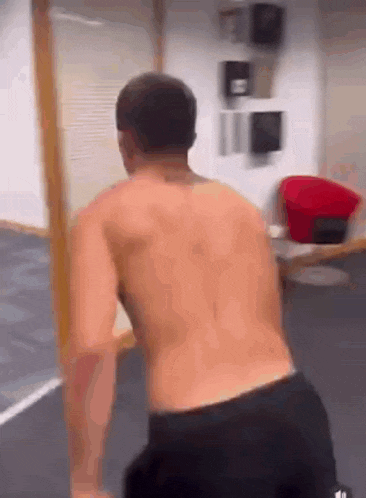 a shirtless man is standing in a room with a red chair in the background .