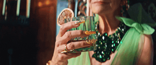 a woman in a green dress is holding a glass of alcohol with a slice of lemon in her hand .