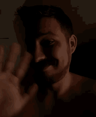 a shirtless man with a beard is making a peace sign with his hand in the dark .
