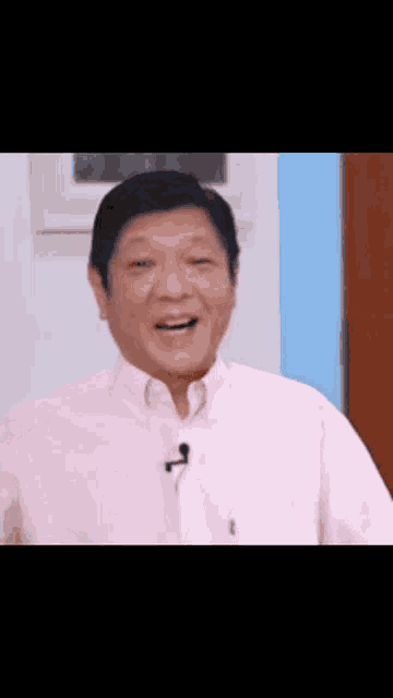 a man in a pink shirt is laughing with a microphone in his mouth .