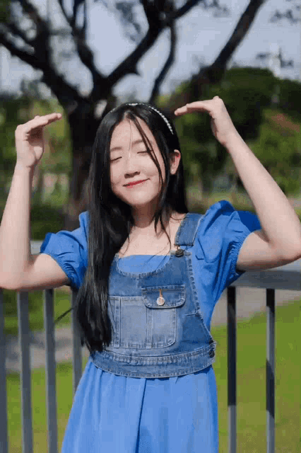 a girl in a blue dress is making a funny face with her hands