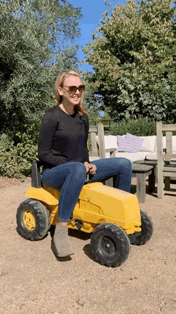a woman in sunglasses is sitting on a yellow toy tractor