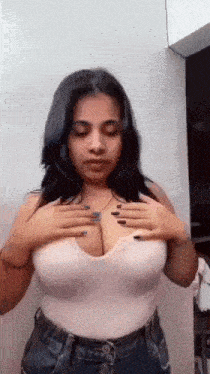 a woman in a white tank top is holding her breasts .