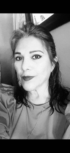 a black and white photo of a woman taking a selfie . she is wearing a necklace and earrings .