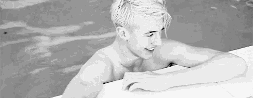 a black and white photo of a shirtless young man leaning on the edge of a swimming pool .