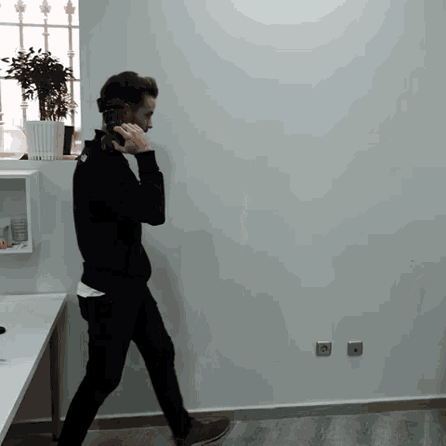 a man in a black sweatshirt is walking and talking on a phone