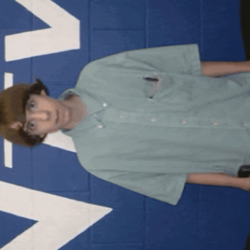 a man in a green shirt is standing in front of a blue wall with a white arrow pointing to the left