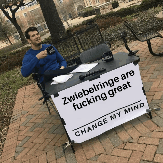 a man is sitting at a table with a sign that says change my mind