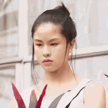 a young woman with her hair in a bun is standing in front of a window and looking at the camera .