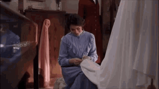 a woman in a blue dress is sewing a white dress in a room .