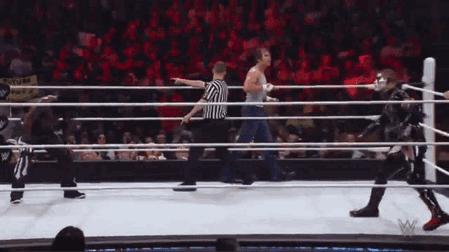 a referee stands in the middle of a wrestling ring with two wrestlers in it
