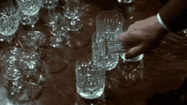 a hand is reaching for a glass of water on a table full of glasses