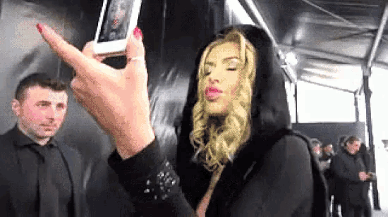 a woman is taking a selfie with her cell phone while a man stands behind her .