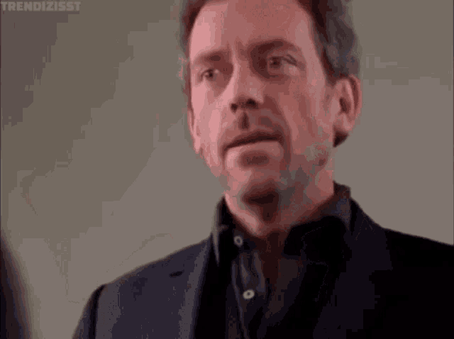 a man in a suit is covering his face with his hand and making a funny face .