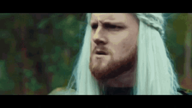 a man with a beard and white hair is wearing a wig and making a funny face .