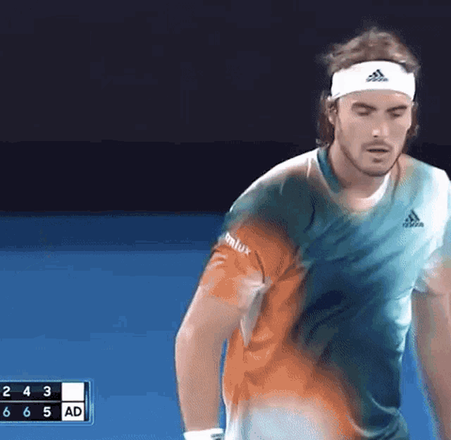 a man wearing a headband and a colorful shirt is playing tennis on a blue court .