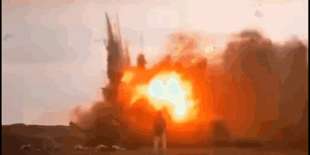 a man is standing in front of a large explosion in the middle of a field .