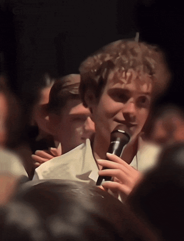 a man in a white shirt is holding a microphone in a crowd