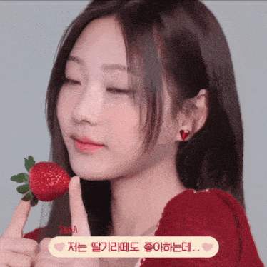 a woman in a red sweater is holding a strawberry to her mouth