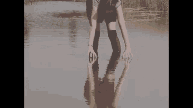 a woman is standing in a body of water with her hands in the water .