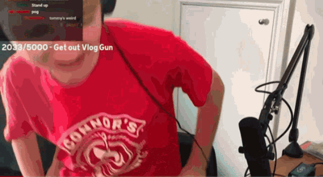 a man wearing a red connor 's t-shirt is standing in front of a microphone