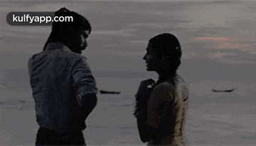 a man and a woman are standing next to each other on the beach looking at each other .