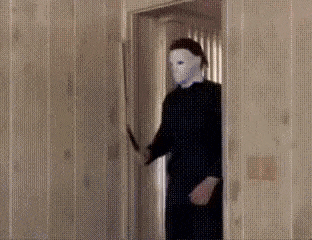 a man in a mask is holding a knife in his hand and standing in a doorway .