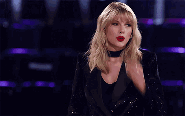 a woman wearing a black tuxedo and red lipstick applauds