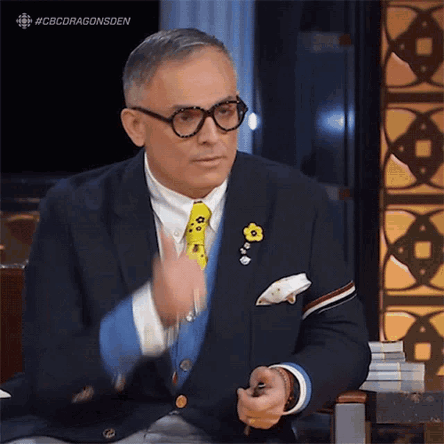 a man wearing glasses and a tie is sitting in a chair with the hashtag #cbcdragonsden above him