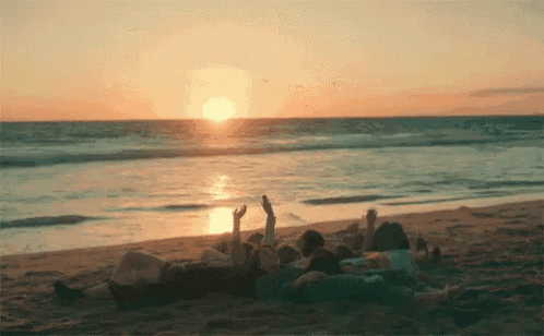 a group of people laying on the beach with their arms in the air