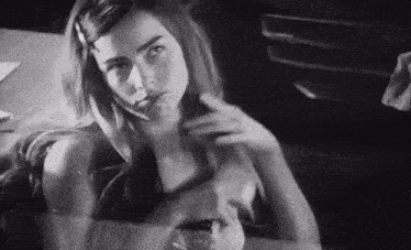 a black and white photo of a woman sitting at a table with her hair in a ponytail .