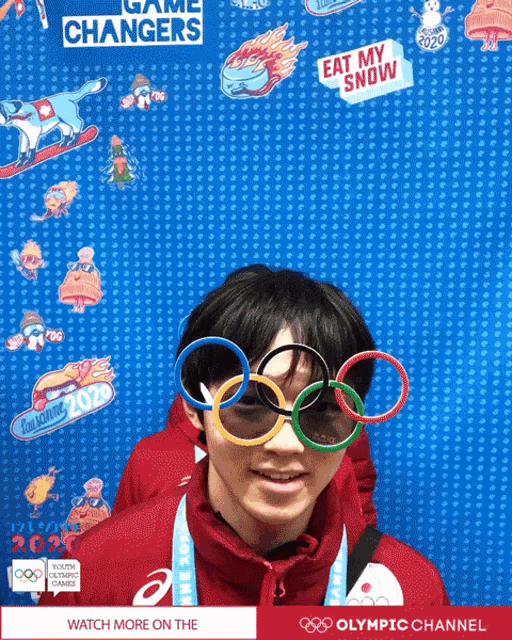 a boy wearing olympic rings glasses stands in front of a wall that says game changers on it