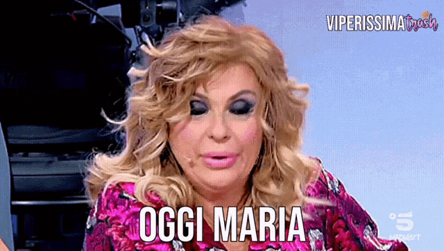 a woman in a pink dress says " oggi maria " in front of a camera
