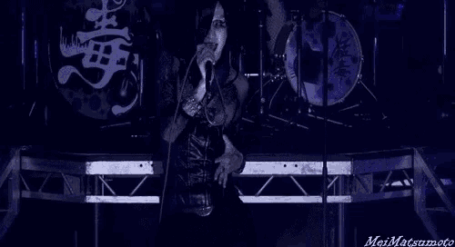 a woman is singing into a microphone on a stage in front of a drum kit .