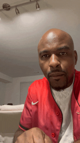 a bald man wearing a red nike jacket looks at the camera