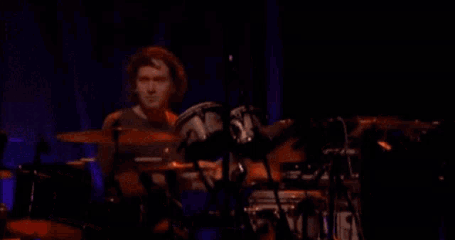 a man is playing drums on a stage in front of a purple background