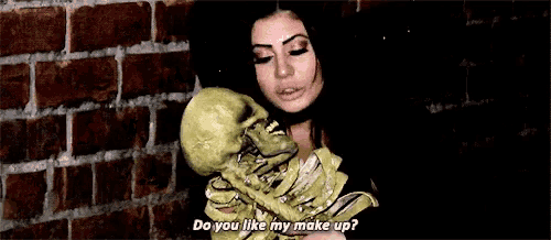 a woman is holding a skeleton and says `` do you like my make up ? ''