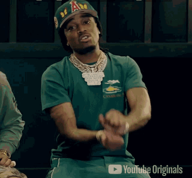 a man wearing a green shirt and a hat with the letter a on it