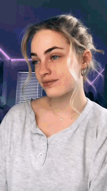 a woman wearing a gray shirt and hoop earrings is looking at the camera