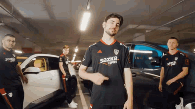 a man wearing a sazka shirt is pointing at something in front of a car