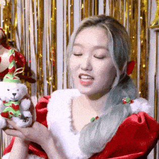 a woman in a santa claus costume is holding a teddy bear in her hands .