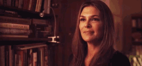 a woman is standing in front of a bookshelf and smiling .